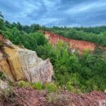 View of Providence Canyon with multicolored cliffs and lush green forest under a cloudy sky.