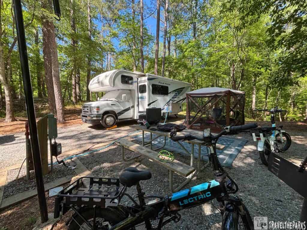 A campsite at Red Top Mountain State Park featuring a parked RV, a camping gazebo, a picnic table, and bicycles, all surrounded by trees.