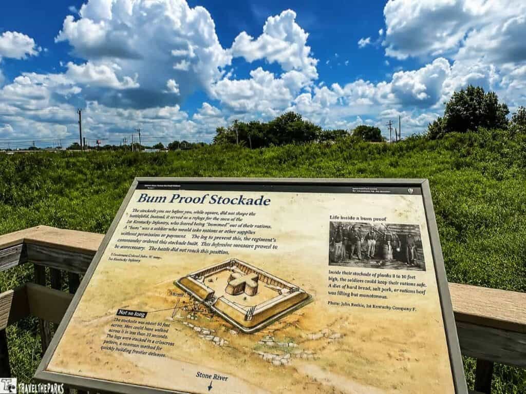 An interpretive sign about the Bum Proof Stockade at Stones River Redoubt-Brannan, featuring an illustration of the fortification layout, surrounded by green grass and a blue sky with clouds.

Transcribed Text:

"Bum Proof Stockade

The stockade you see before you, while sturdy, did not change the fortifying business in a sense as a refuge for the needs of the 1st Kentucky Infantry. It is often being “bummed” out of their route. A ‘bum’ is a soldier who would take rations or other supplies without permission or payment. The log to prevent this, the regiment’s commander ordered this stockade built. This defensive measure proved to be unnecessary.