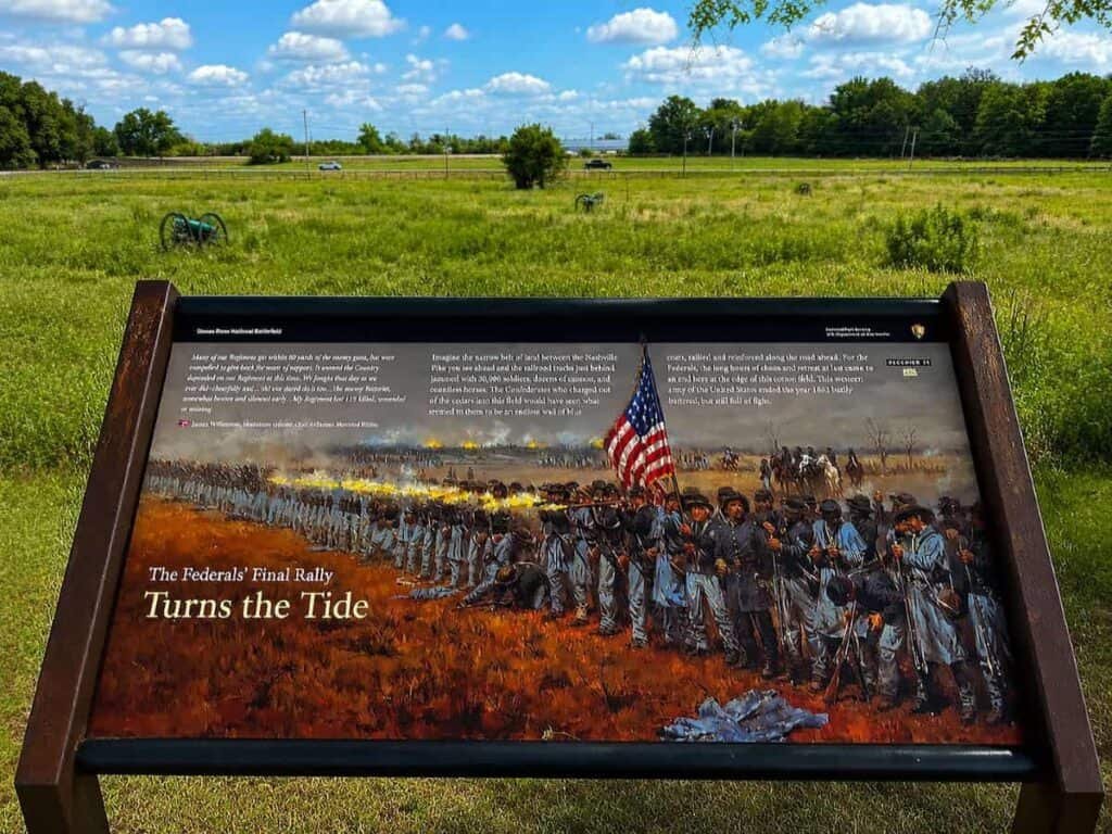 Illustrated historical plaque depicting Union soldiers in battle at Stones River National Battlefield, with a fiery background and clear sky.

