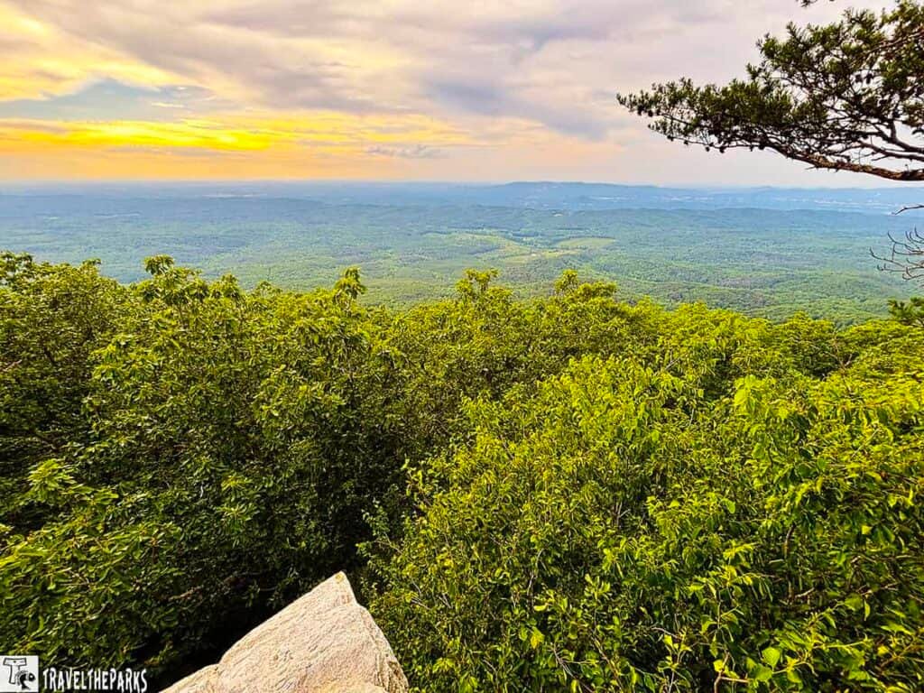 A panoramic view from a high point in Talladega National Forest, featuring green foliage, rolling hills, and a colorful sky at sunset or sunrise.