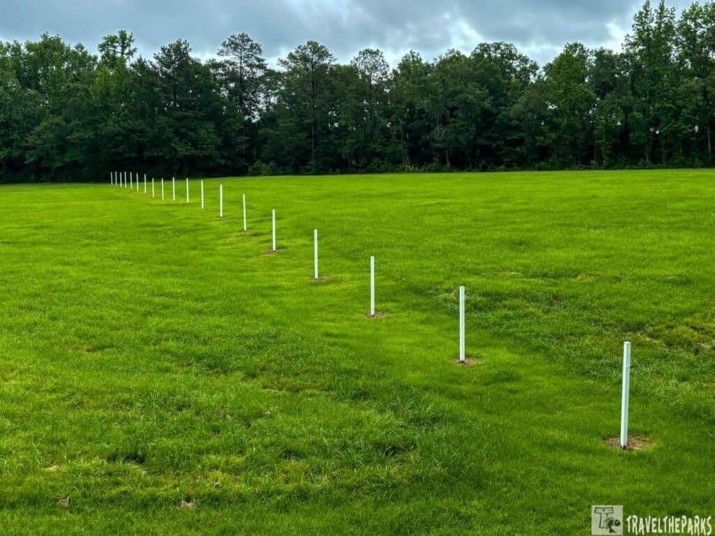 A series of white posts lined up in a green field at Horseshoe Bend National Military Park, with trees in the background under a cloudy sky.