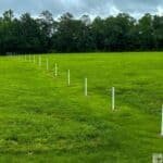 A series of white posts lined up in a green field at Horseshoe Bend National Military Park, with trees in the background under a cloudy sky.