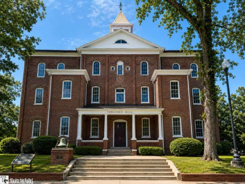 Thrasher Hall at Tuskegee Institute, a three-story red brick building with a white-trimmed facade, columns, and a triangular gable, surrounded by greenery under a bright blue sky.