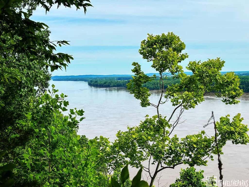 A scenic view from Trail of Tears State Park, featuring green foliage framing a tranquil river and distant hills under a blue sky.