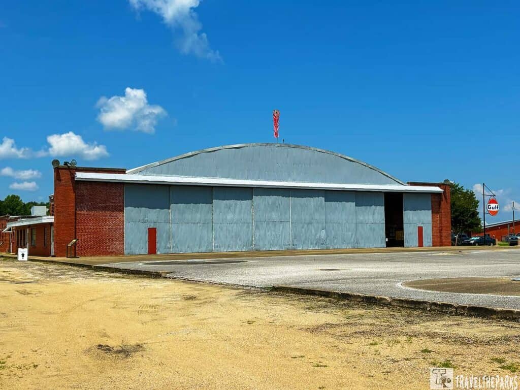 Red brick building with an arched gray roof at the Tuskegee Airmen National Historic Site, surrounded by green grass and an airstrip in the background.