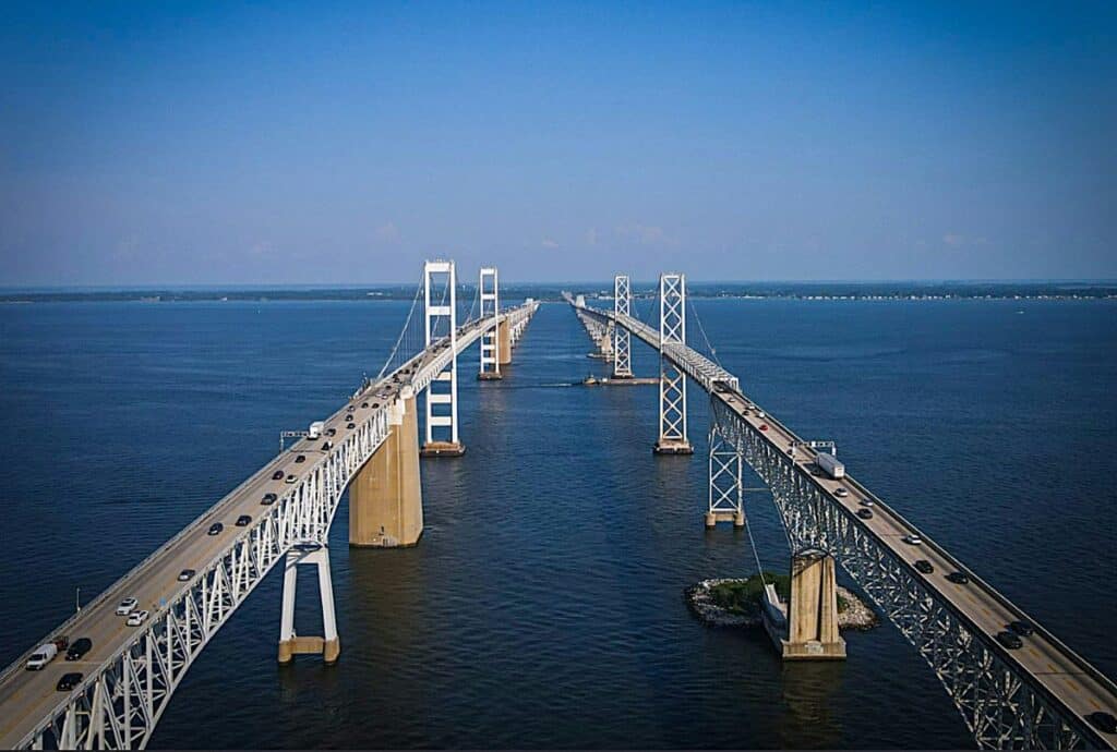 Virginia Scenic Byways: Aerial view of the Chesapeake Bay Bridge, featuring two main spans over blue water, with vehicles traveling on multiple lanes.