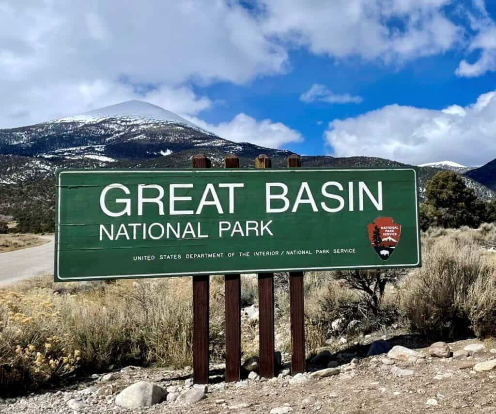 Green sign for Great Basin National Park against a mountain backdrop, featuring bold white text and the National Park Service logo.

