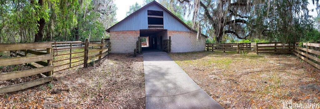 View of a pathway leading through a rustic building at La Chua Trail, surrounded by a wooden fence and lush greenery.