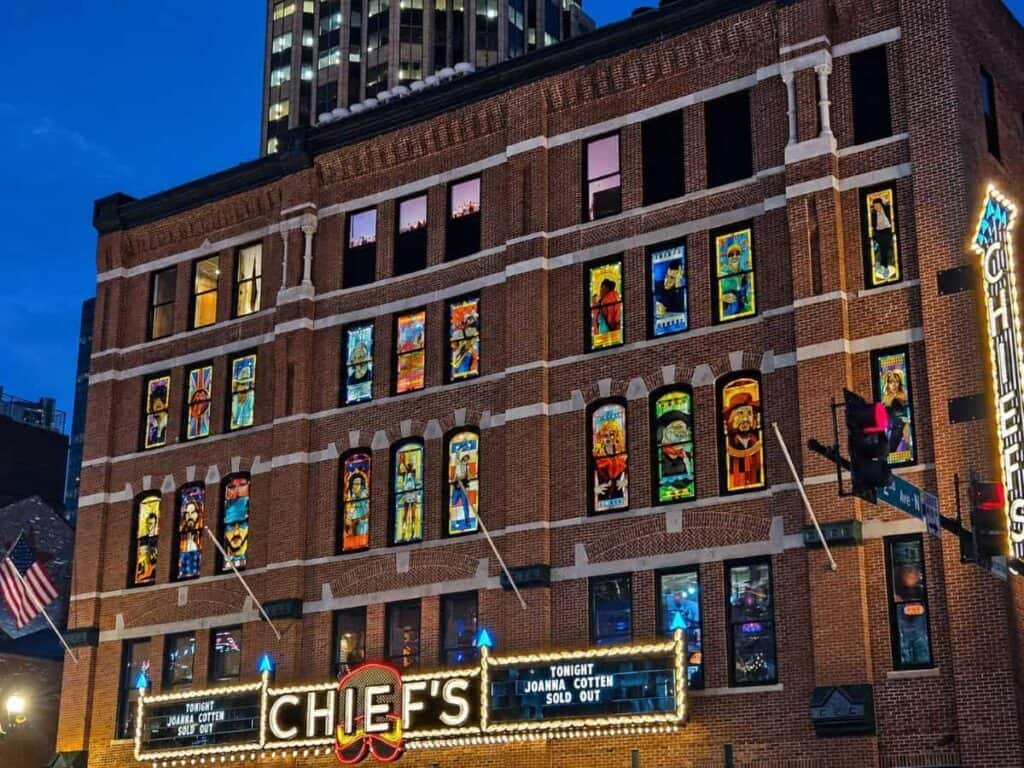 A historic brick building at dusk featuring colorful stained glass windows and a marquee sign that reads "CHIEF'S" advertising a sold-out event.

