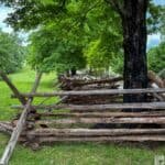 Wooden split-rail fence at Fort Donelson National Battlefield, surrounded by grass and trees under a cloudy sky.