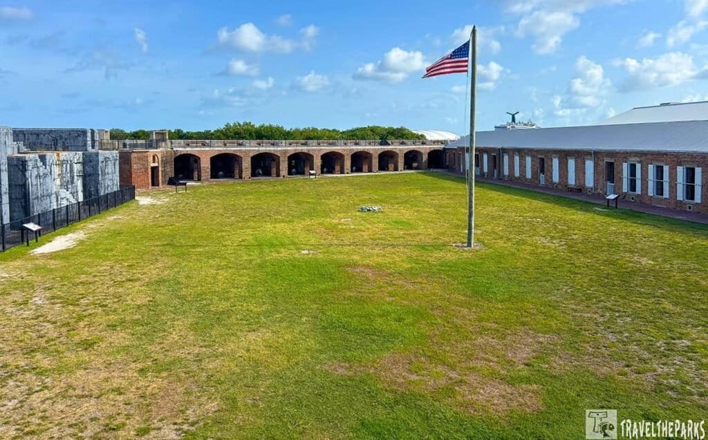 A historic fort at Fort Zachary Taylor State Park with a green lawn in front, an American flag on a pole, and brick structures with arched doorways under a clear sky.
