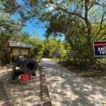 Entrance to Fort Zachary Taylor Historic State Park with a cannon, informational sign, and path lined by trees.