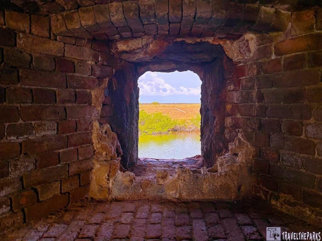 View from a brick window in Fort Zachary Taylor, framing greenery and water under a partly cloudy sky.