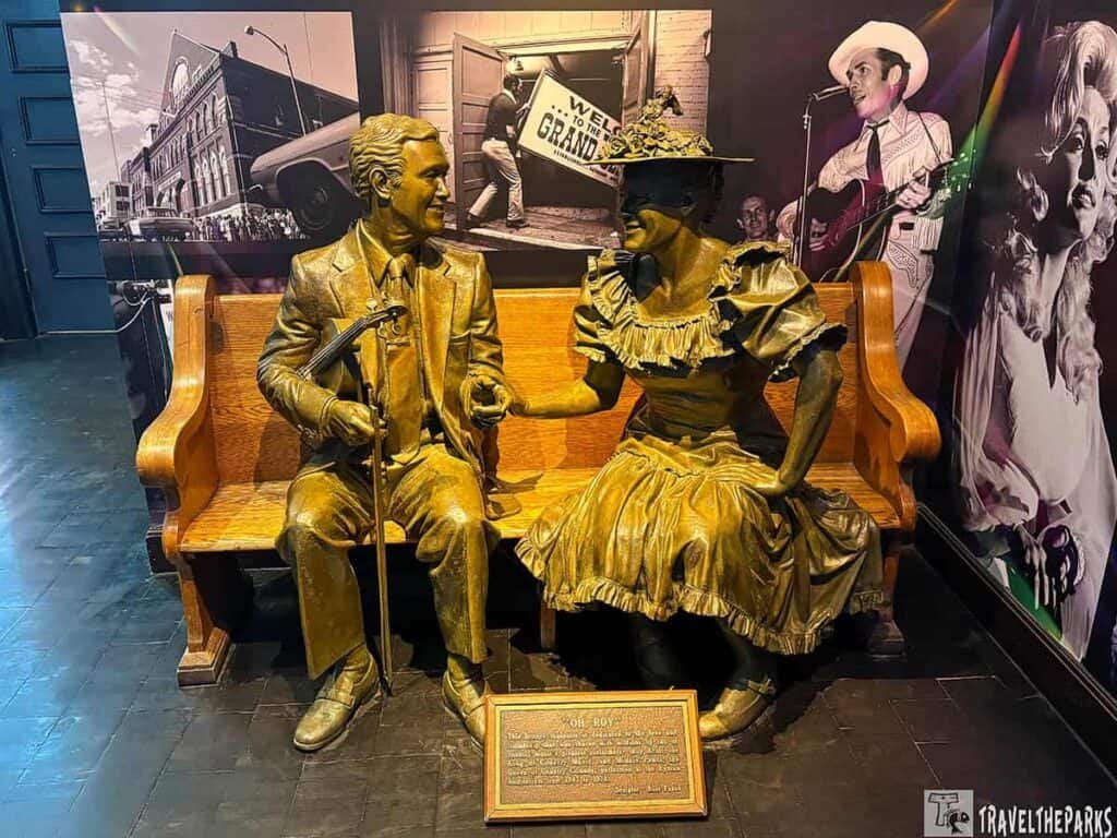 Ryman Auditorium, Nashville, Tennessee. Bronze statues of a Roy Acuff with a violin and a Minnie Pearl in a dress sitting on a wooden bench with a plaque in front.
