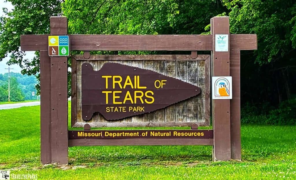 Sign marking the Trail of Tears State Park, featuring an arrowhead shape and surrounded by green foliage, with symbols for activities and rules.
