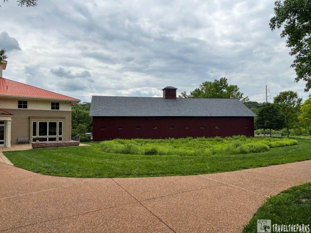 View of the Ulysses S. Grant Museum featuring a modern building with a red metal roof and an adjacent red barn, set in a green landscape under a cloudy sky.