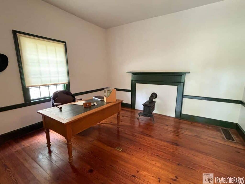 Interior view of Ulysses S. Grant's office featuring a wooden desk, chair, window with shade, and a cast iron stove, all in a historically styled room.