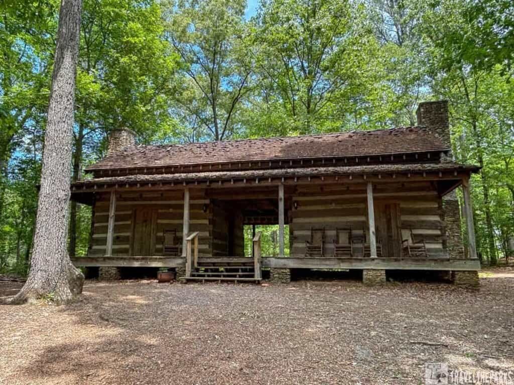 Rustic Vaugn Cabin in Red Top Mountain State Park, featuring a log construction with a porch and rocking chairs, set among greenery.

