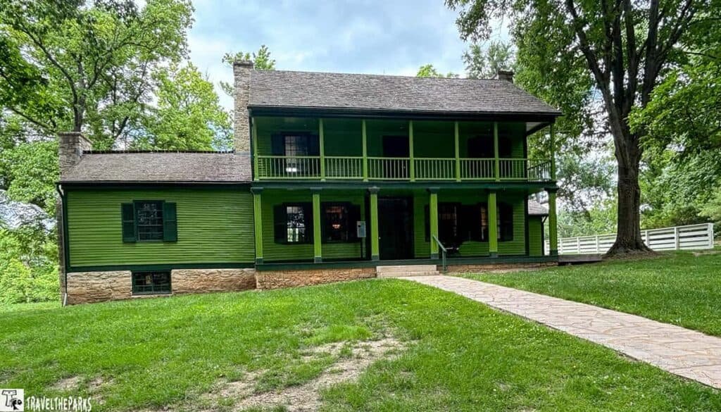 Historic two-story green house with a porch, large tree, and stone chimney at Ulysses S. Grant National Historic Site.