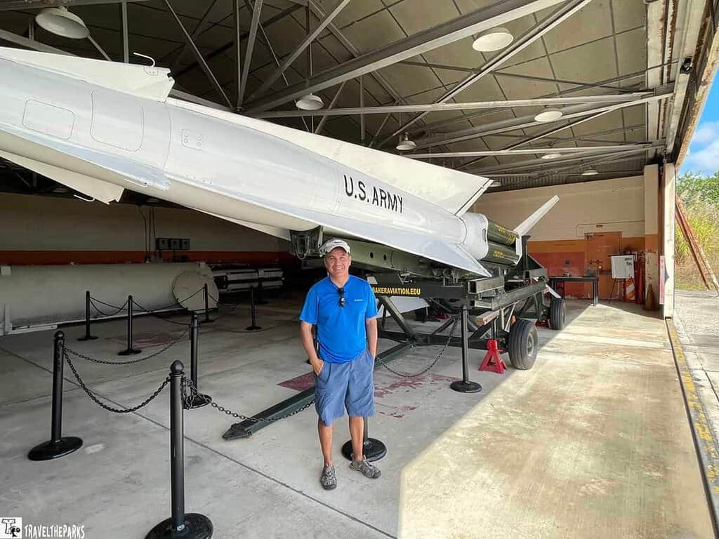 Interior view of the HM-69 Nike Missile Site, featuring a white Nike missile on a launch platform with a person standing beside it, surrounded by stanchions and industrial elements.