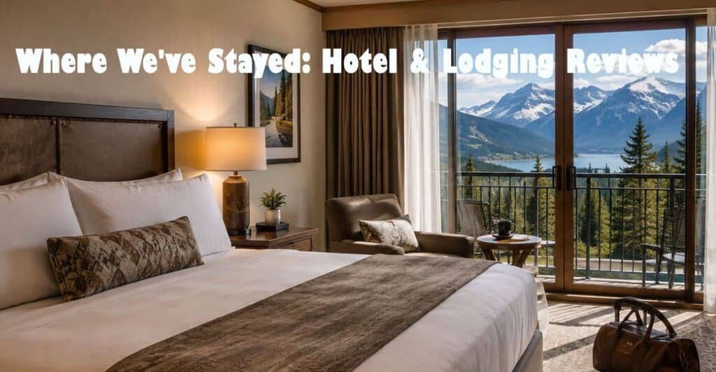 A cozy hotel room featuring a large bed, a decorative pillow, a bedside lamp, and a view of mountains through floor-to-ceiling windows.