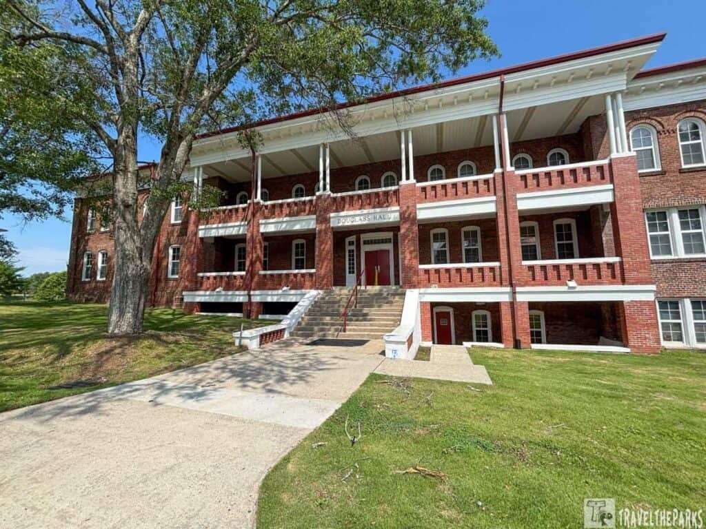 Exterior view of Douglass Hall at Tuskegee Institute, showcasing red brick architecture, a wide staircase, and a large tree on a green lawn.

